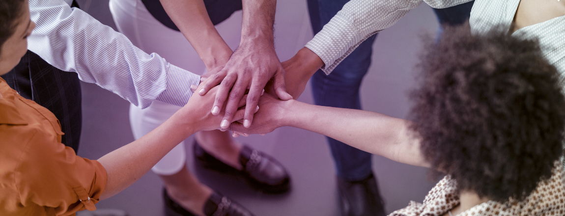 uma roda pessoas com as mãos sobrepostas, simbolizando apoio